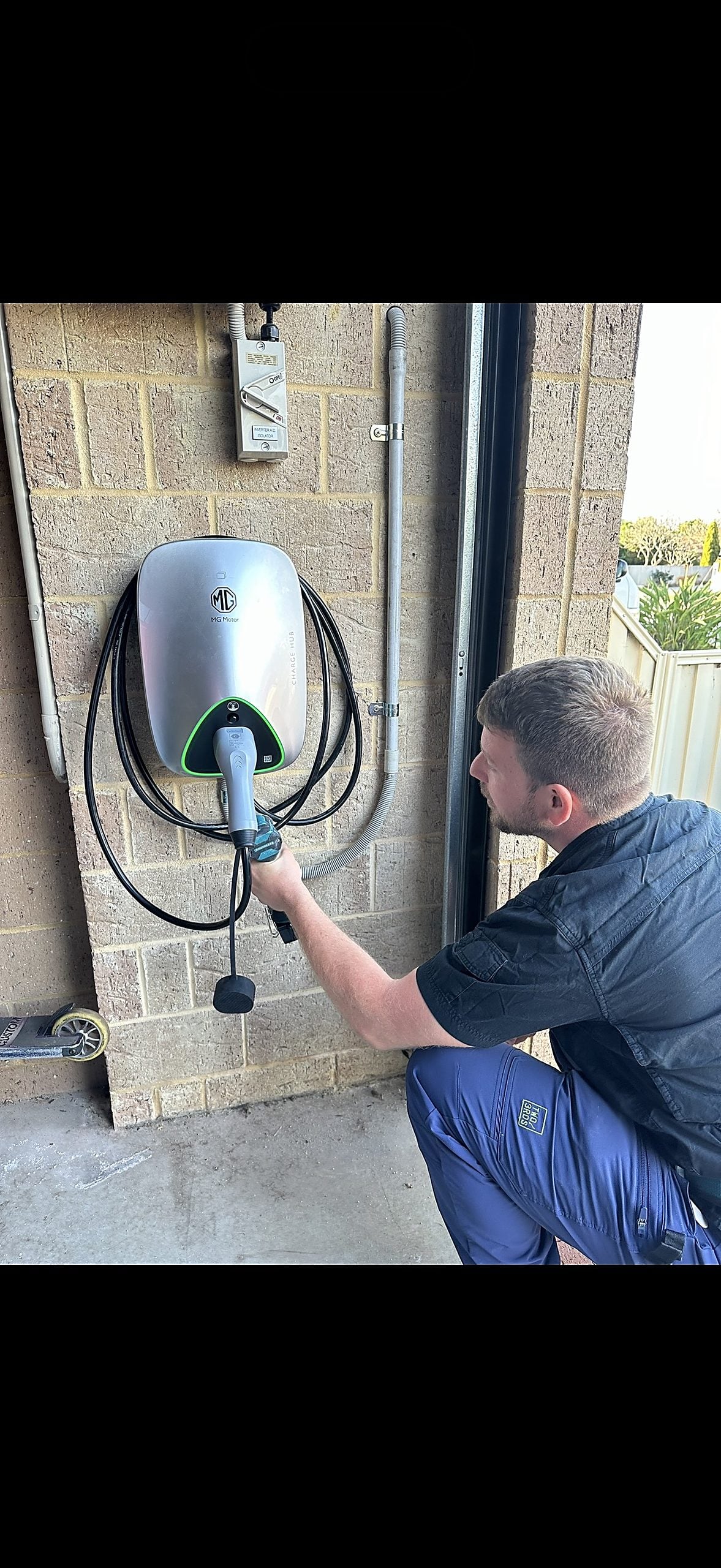 Riverside electrician plugging a lead into a wall-mounted EV charger on a brick home in Perth