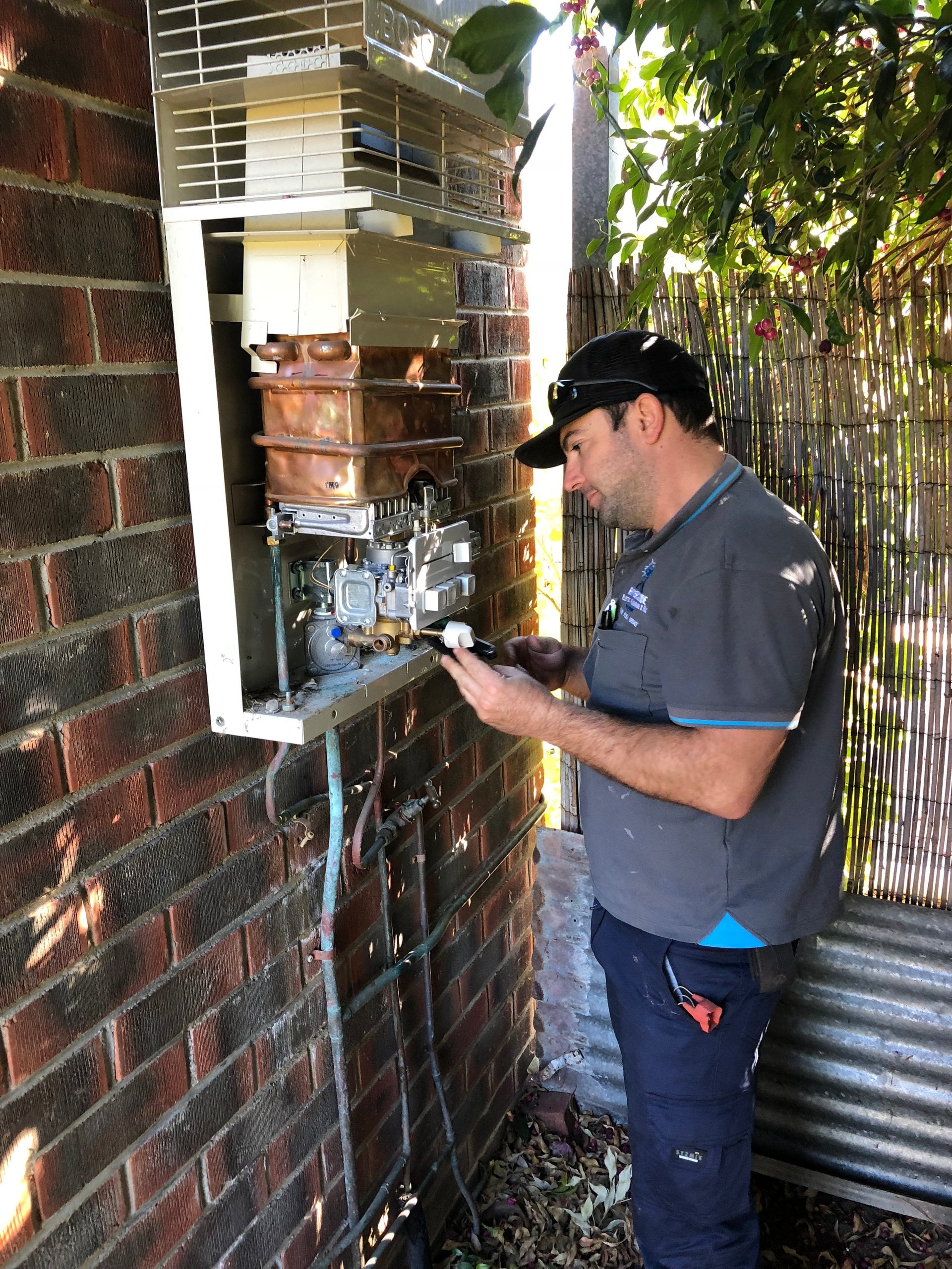 Riverside gas fitter servicing a continuous flow gas hot water unit on a brick wall