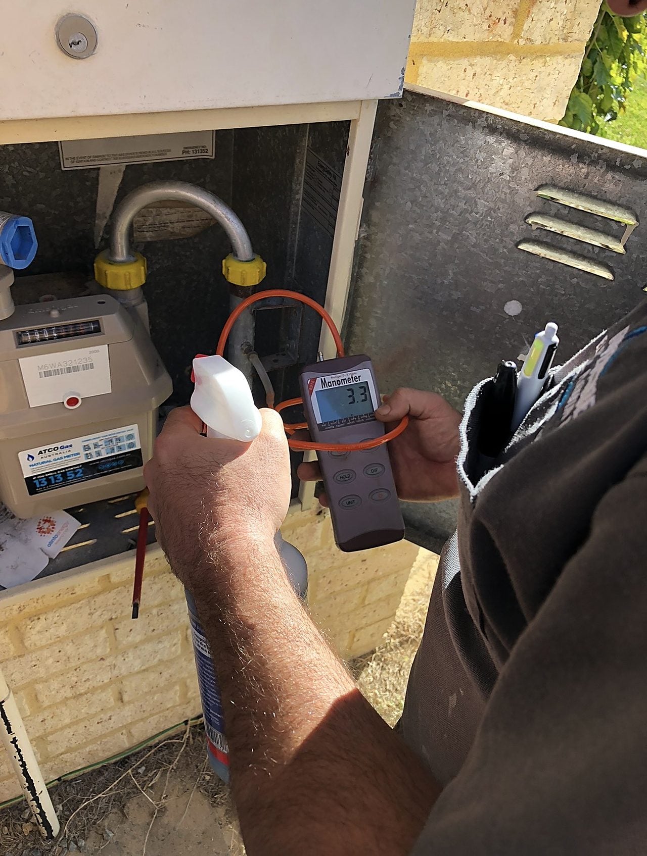 A gas fitter leak-testing a gas meter connection with a detector