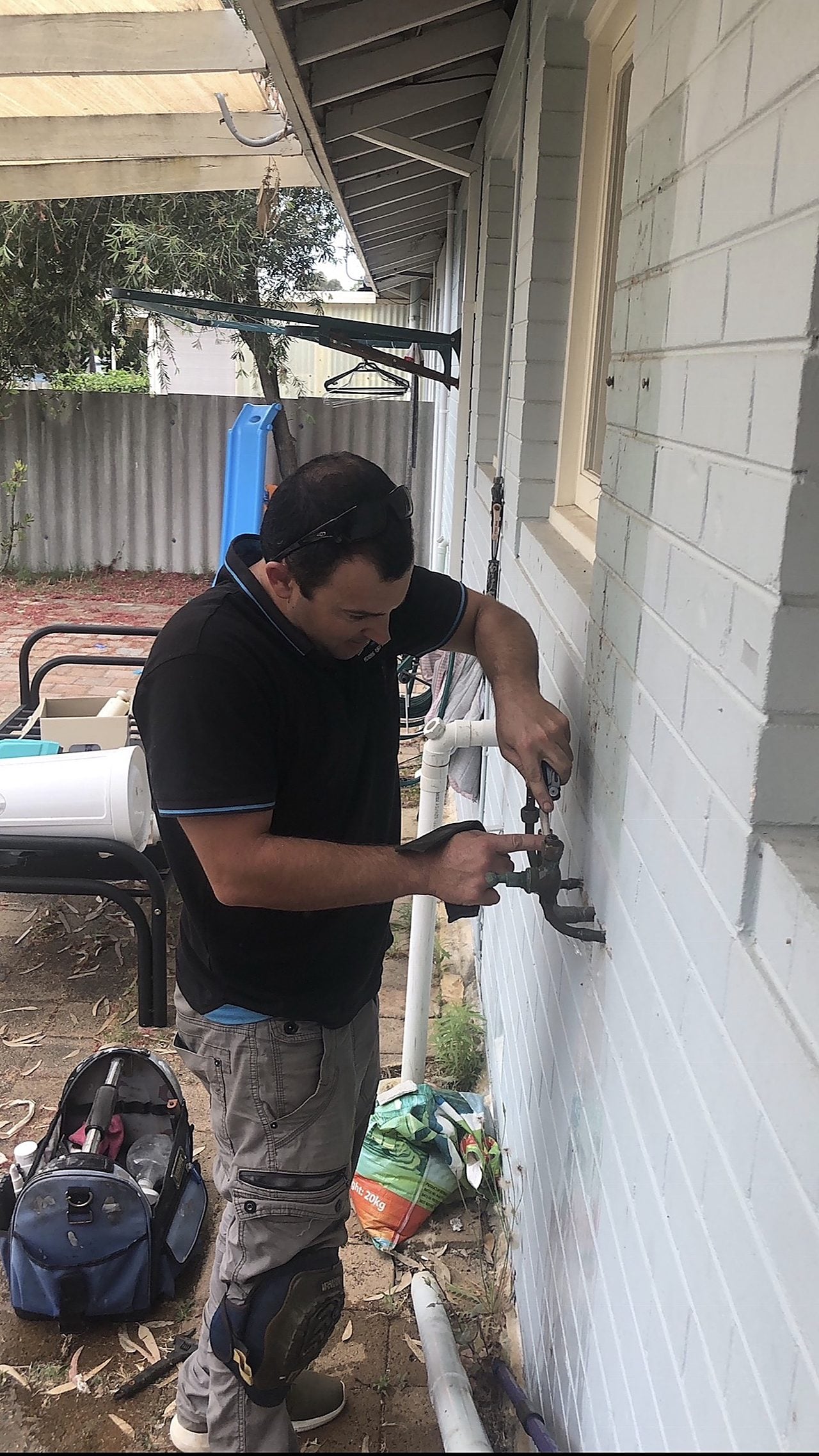 A Riverside plumber repairing a water leak on the outside wall of a Perth home